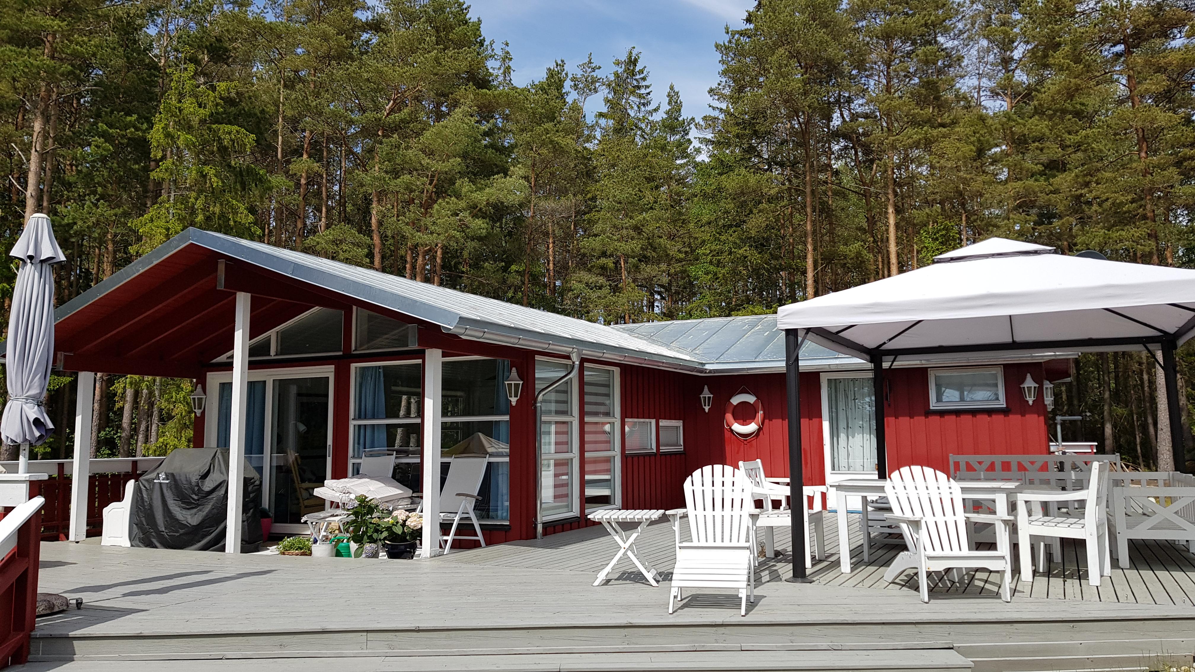 Rød hytte med hvitt, båndtekket sinktak og terrasse